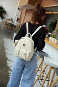 Detailansicht eines weißen PU-Lederrucksacks mit süßem Teddybär-Anhänger und Blumenverschluss