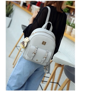 Detail eines grauen PU-Lederrucksacks mit Bärenanhänger und Blumenschnalle am Modell