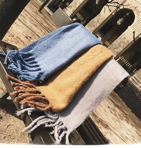 Close-up of thick mohair knitted scarves with long tassels in navy, yellow and grey colors