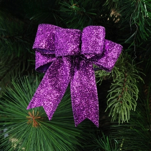 Close-up of a 10cm purple glitter bow tie ornament on a green Christmas tree branch