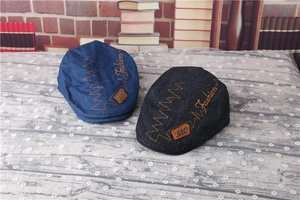 Detail of blue and black denim flat caps with embroidered Fashion text and leather patch