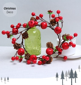 Close-up of a Christmas wreath with red berries and pine cones around a glass bottle