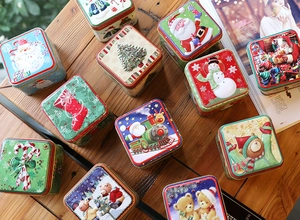Detailed view of square Christmas tin boxes featuring Santa and Snowman festive patterns