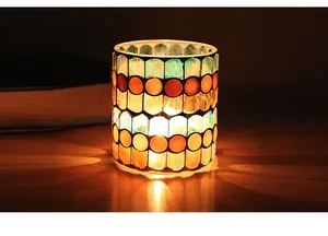 Detail of mosaic glass candle holder with warm light through green and orange tiles