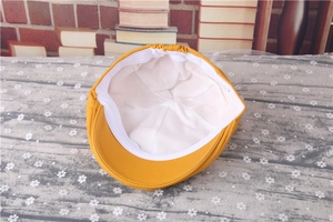 Detail view of yellow striped baby beret cap showing white cotton lining and soft inner texture