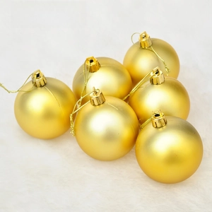Detail of matte gold Christmas ornaments with hooks on a soft white plush surface