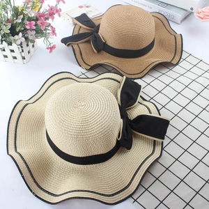 Top view of two woven straw hats with black wavy edges and large ribbon bows for summer