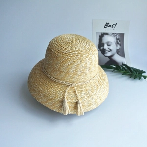 Detailed macro view of woven natural straw fibers and tassel accents on the cloche sun hat