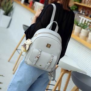 Detail eines grauen PU-Lederrucksacks mit Blumenschnallen und süßem Bärenanhänger