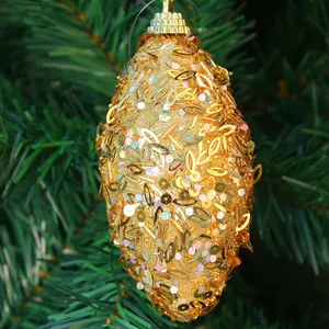 Detail of 11cm gold sequined oval Christmas ball ornament hanging on a pine tree branch