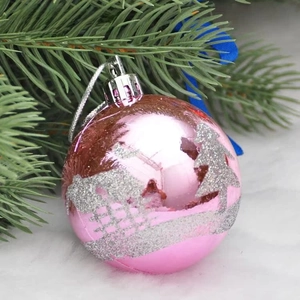 Pink Christmas ball ornament with silver glitter tree and house motifs on a pine branch