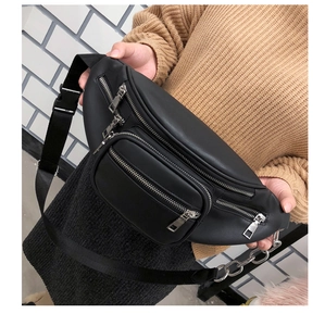 Close-up of black leather chest bag with silver zippers and metal chain strap detail