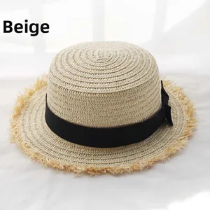Detailed macro view of the beige raffia hat featuring a black ribbon bow and fringed edges