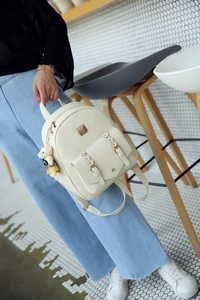Detailansicht eines weißen PU-Lederrucksacks mit goldenen Beschlägen und Bären-Anhänger