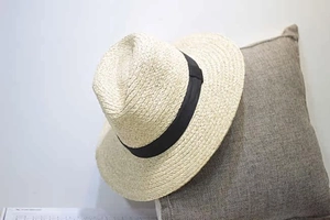 Detail of raffia sun hat with black ribbon placed on a textured indoor cushion