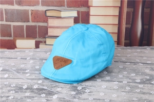 Detail of bright blue baby flat cap with WBK leather patch on a lace tablecloth