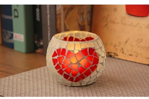 Close-up of mosaic glass candle holder with red heart pattern and warm candle glow