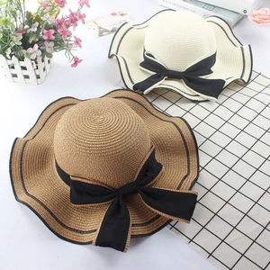 Detail of woven straw hats featuring chic black bow ribbons and wavy contrast edges