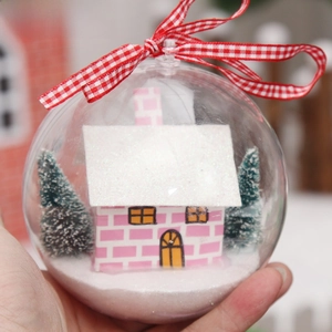 Close-up of a clear Christmas ball featuring a pink miniature house and tiny snow trees