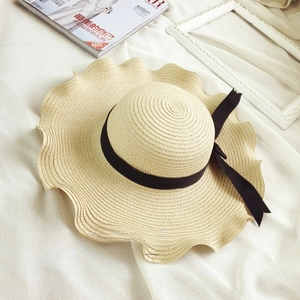 Detail of woven beige straw sun hat with wide wavy brim and elegant black bow ribbon