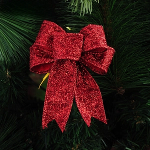 Detail of red glitter Christmas bow hanging on a green pine branch background
