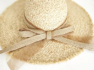 Detailansicht eines beigen Raffia-Strohhuts mit ausgefranstem Rand und Chiffon-Schleife