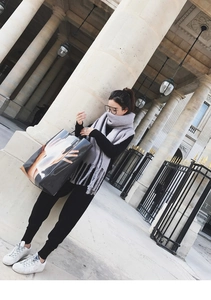 Detail of light grey knit mohair scarf with tassels paired with a glossy graphic tote bag