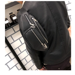 Detail of a black faux leather waist bag with three silver zippers worn as a crossbody bag