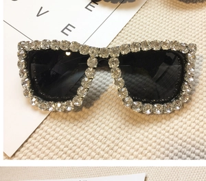 Detail of fashion oversized sunglasses with silver rhinestones on ivory woven background