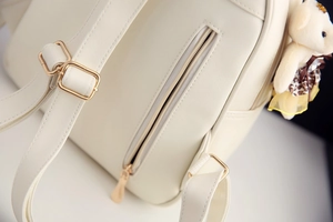 Detail eines weißen PU-Lederrucksacks mit goldenem Reißverschluss und Bärenanhänger