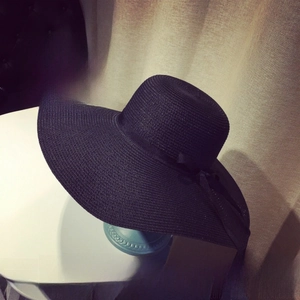 Detail of a black wide-brim straw hat with a matching ribbon bow and fine weave