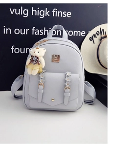 Detail eines hellgrauen PU-Rucksacks mit Bärenanhänger und floralen Zierriemen