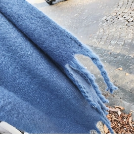Close-up of fluffy dark blue mohair scarf featuring long tassels on a stone background
