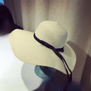 Close-up of beige straw sun hat featuring delicate woven texture and black ribbon bow