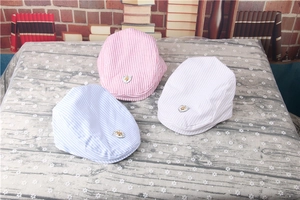 Detailed close-up of striped baby berets in pink, light blue, and beige with metal shields