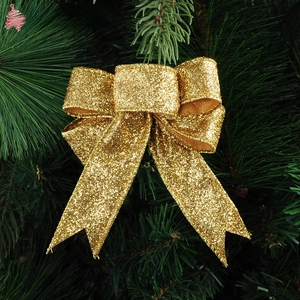 Close-up of sparkling 10cm gold glitter Christmas bow ornament on green pine branches