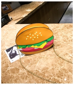 Detail of creative hamburger shaped shoulder bag with golden chain on marble surface