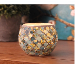 Macro shot of mosaic glass candle holder with fish scale patterns and warm glowing candle
