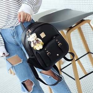 Detail eines schwarzen Lederrucksacks mit Metallplakette und süßem Bärenanhänger