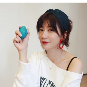 Detail of the blue egg-shaped makeup sponge held by a model in a casual white hoodie