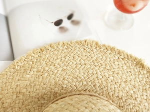 Detail eines Raffia-Sonnenhuts mit Fransenrand, gestylt mit Magazin und Getränk
