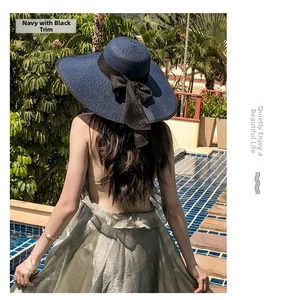 Detail of wide brim navy straw hat with black ribbon and bow by a poolside palm scene