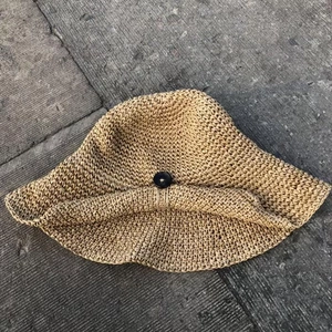Detail of hand-woven straw sun hat with decorative black button and textured weave pattern