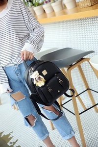 Detail eines schwarzen PU-Lederrucksacks mit Goldschnalle und Bärenanhänger am Model
