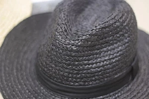 Close-up of the black raffia fedora showing the fine woven texture and decorative band