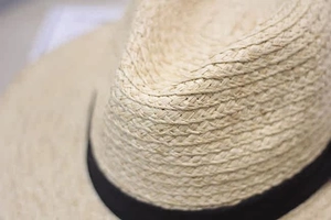 Close-up of beige raffia straw hat showing detailed weave texture and black ribbon