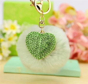 Detail of light green fluffy pompom and heart rhinestone pendant on gold keychain
