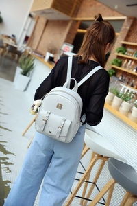 Hellgrauer PU-Rucksack mit Blumenschnalle und Plüsch-Anhänger im modernen Café