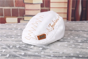 Detailed close-up of white striped beret with brown Fashion embroidery and 1987 leather patch