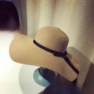 Close-up of wide brim straw sun hat with elegant black ribbon bow detail on a stand